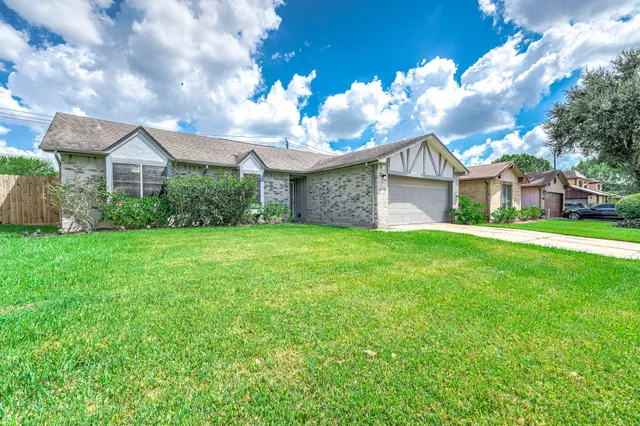 a view of a brick house with a big yard plants and large trees