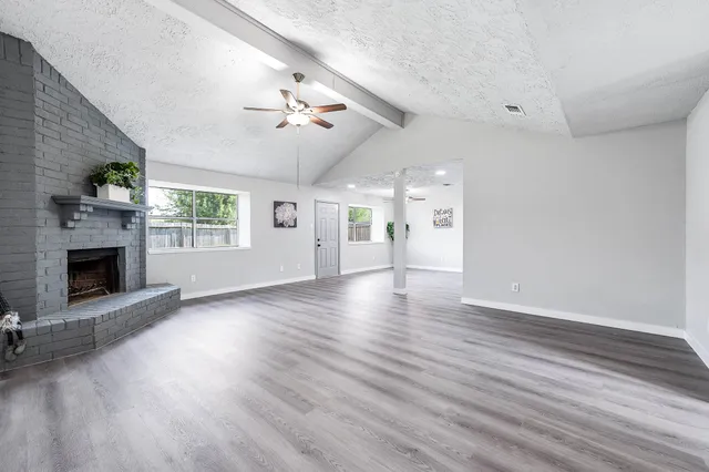 an empty room with windows a fireplace and wooden floor