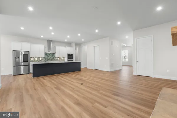 a view of an empty room with wooden floor and a kitchen