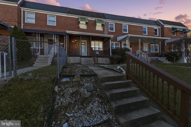 a view of a brick house with large windows and a yard with plants and wooden fence