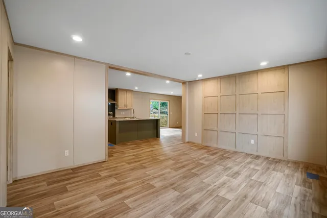 a view of an empty room with wooden floor and a kitchen