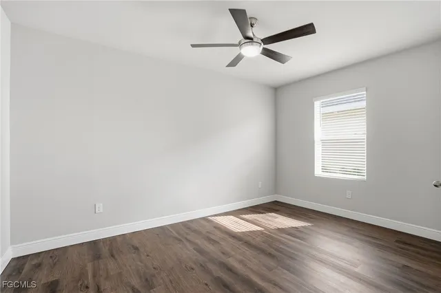 an empty room with wooden floor ceiling fan and windows