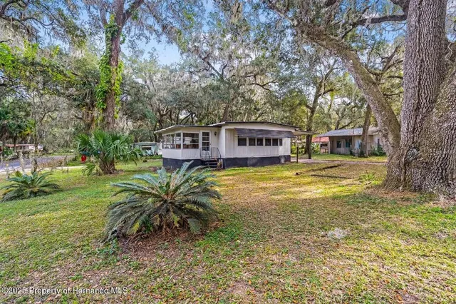 a view of a house with a big yard with plants and large trees
