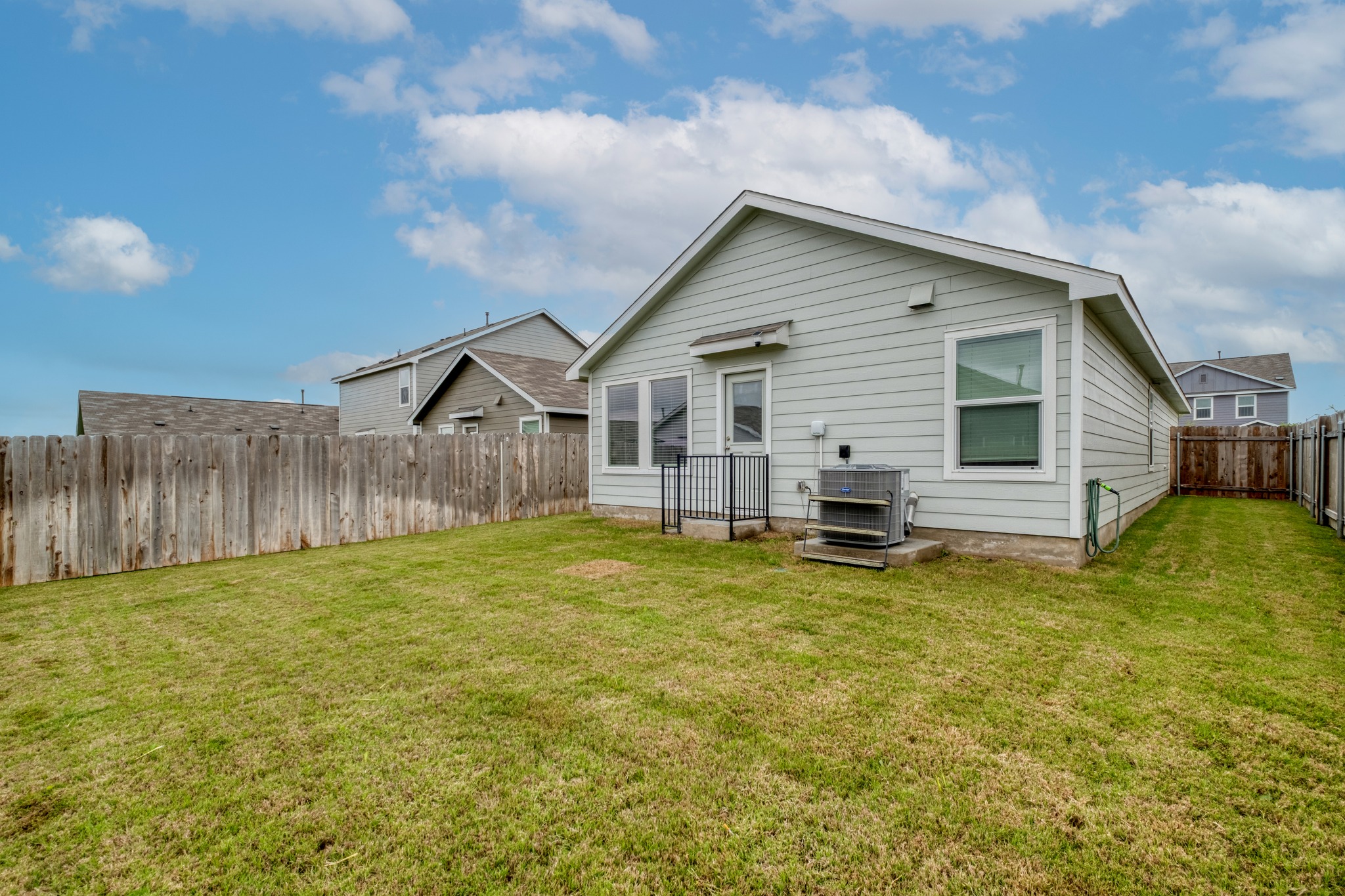 23412 Tiny Moons Way Elgin, TX 78621 - Photo 37 of 38 Expansive grassy backyard featuring a light gray siding exterior, multiple windows, a rear entry door, and a full perimeter wood fence