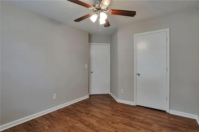 a view of an empty room with wooden floor and a ceiling fan