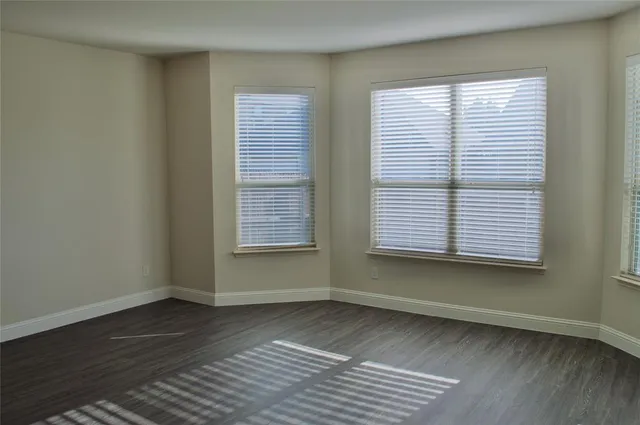 a view of an empty room with wooden floor kitchen view and a window