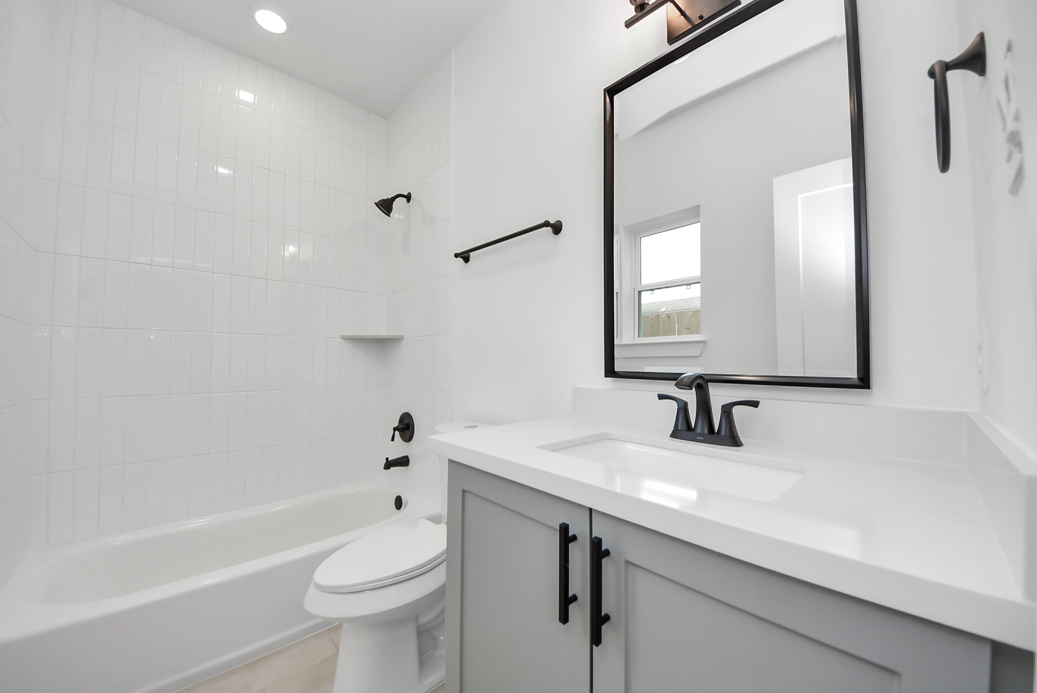 927 Fisher Street, Unit B Houston, TX 77018 - Photo 40 of 47 This bathroom features a clean, modern design with white tile, a bathtub-shower combination, and a sleek vanity with a large mirror. Black fixtures add a stylish contrast, creating a bright and contemporary space.