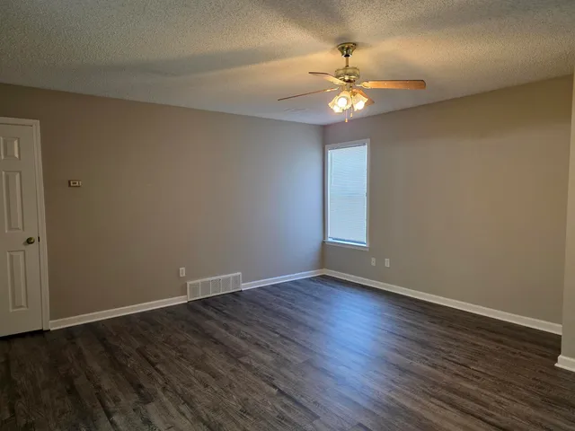 a view of an empty room with wooden floor and a ceiling fan