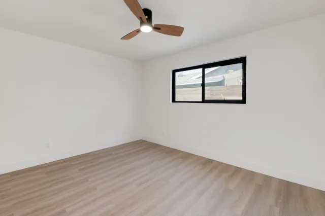 a view of an empty room with wooden floor and a ceiling fan
