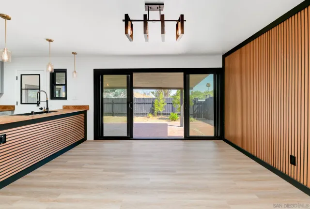 a view of an empty room with window and kitchen view
