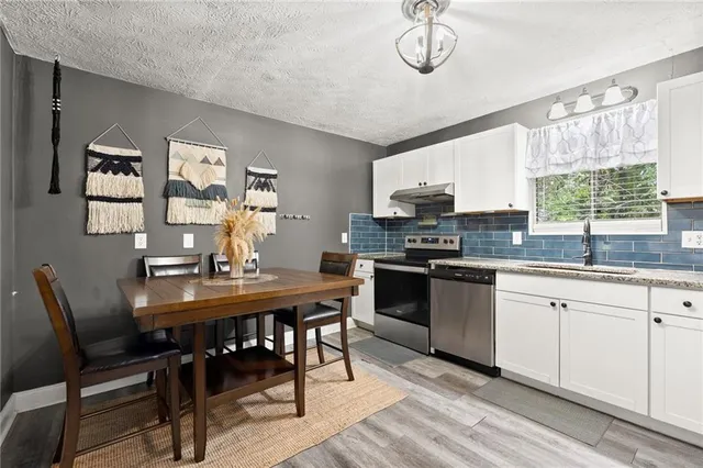 a kitchen with stainless steel appliances granite countertop a stove a refrigerator a microwave a dining table and chairs with wooden floor