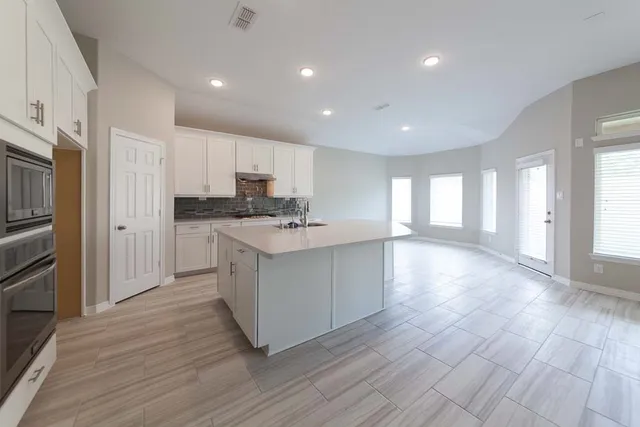 a kitchen with stainless steel appliances granite countertop a stove a sink a refrigerator and white cabinets with wooden floor