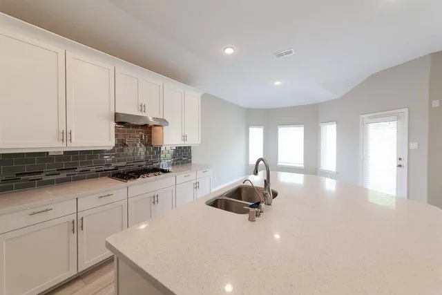 a kitchen with stainless steel appliances a sink a stove a chimney a refrigerator and cabinets