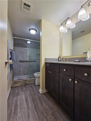 a bathroom with a granite countertop shower a toilet a sink and a mirror