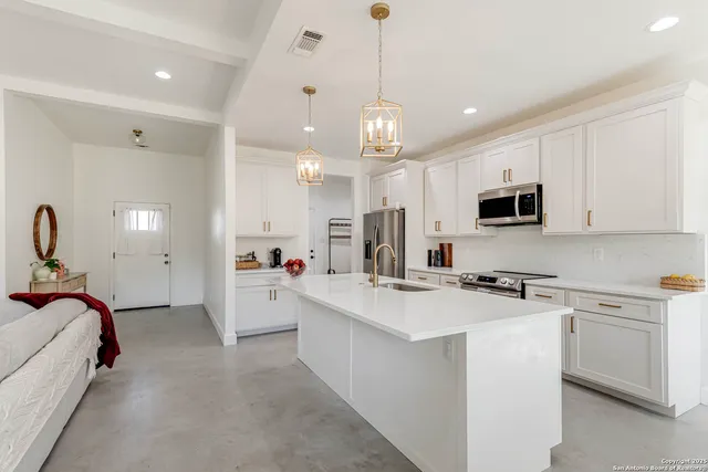 a large white kitchen with lots of counter space a sink appliances and cabinets