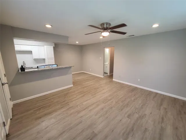 an empty room with wooden floor a ceiling fan and windows