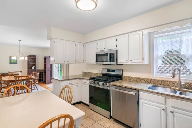 a kitchen with stainless steel appliances granite countertop a stove top oven a sink dishwasher a dining table and chairs with wooden floors