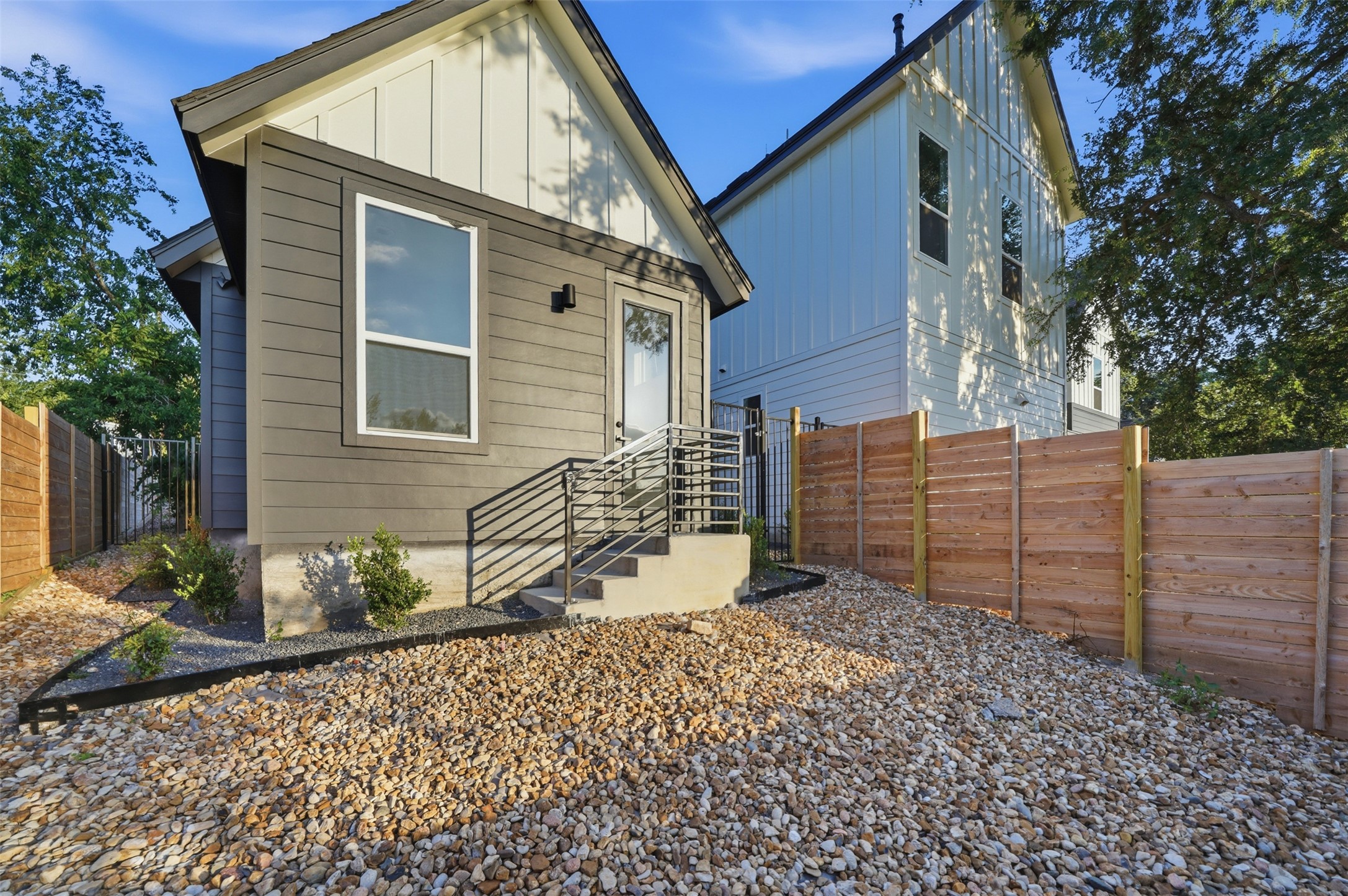 2212 Yellow Jacket Lane, Unit 2 Austin, TX 78741 - Photo 22 of 25 Modern exterior featuring horizontal siding, a gabled roofline, contemporary black railing, a gravel ground covering, and a new wooden privacy fence