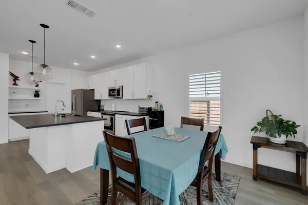 a kitchen with stainless steel appliances kitchen island granite countertop a stove a refrigerator a dining table and chairs with wooden floor