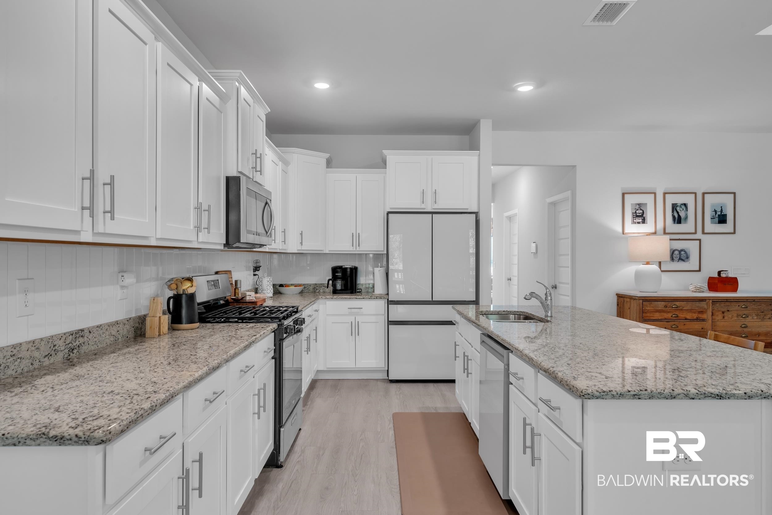 8774 Primland Boulevard Foley, AL 36535 - Photo 13 of 49 Kitchen featuring appliances with stainless steel finishes, a center island with sink, light stone countertops, white cabinets, and light wood-style flooring
