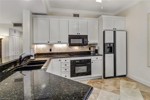 a kitchen with granite countertop a refrigerator stove and white cabinets