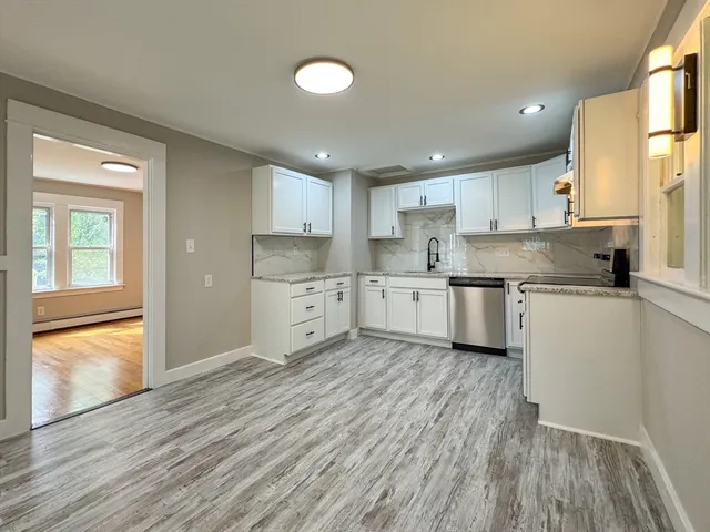 a kitchen with stainless steel appliances granite countertop a stove top oven a sink dishwasher and white cabinets with wooden floor