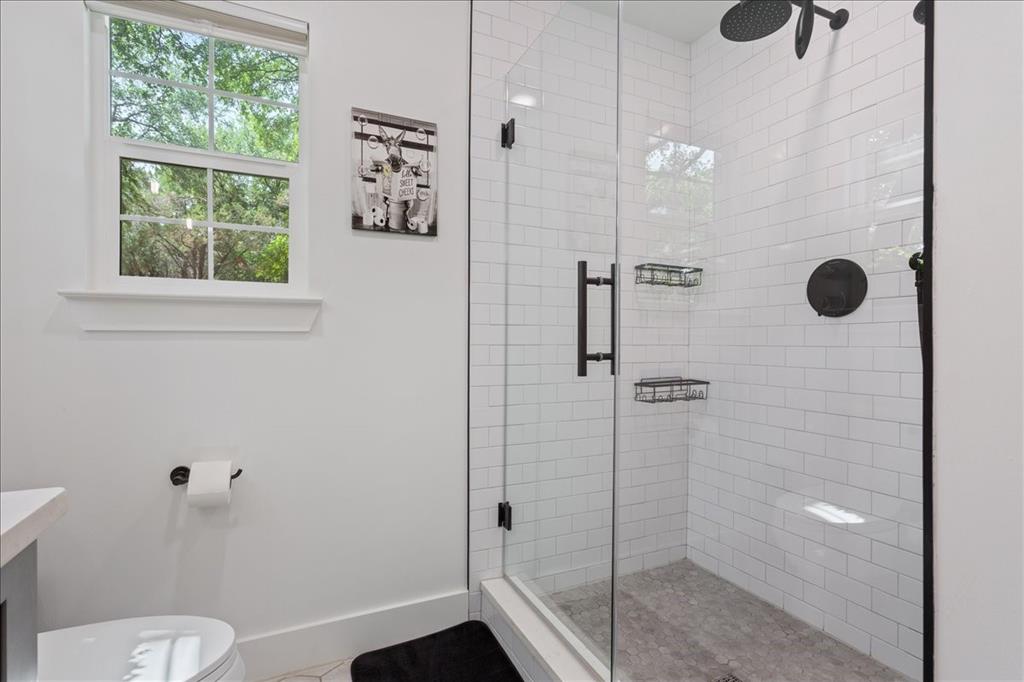 15988 Wortham Bend Road China Spring, TX 76633 - Photo 21 of 40 Walk-in shower featuring a frameless glass enclosure, white subway tile surround, dark-finish fixtures, and a pebble-finish shower pan