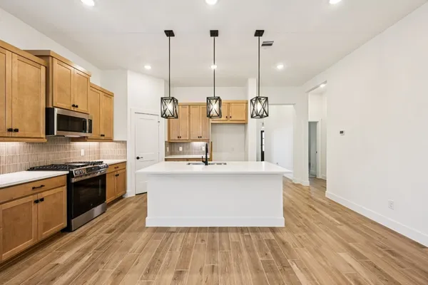 a kitchen with a sink a chandelier stainless steel appliances and cabinets