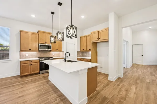 a large kitchen with stainless steel appliances kitchen island granite countertop a stove a sink a refrigerator and white cabinets with wooden floor