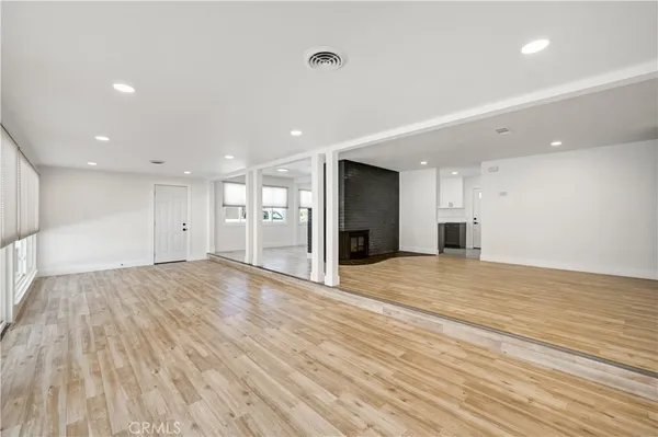 a view of an empty room with wooden floor and a kitchen