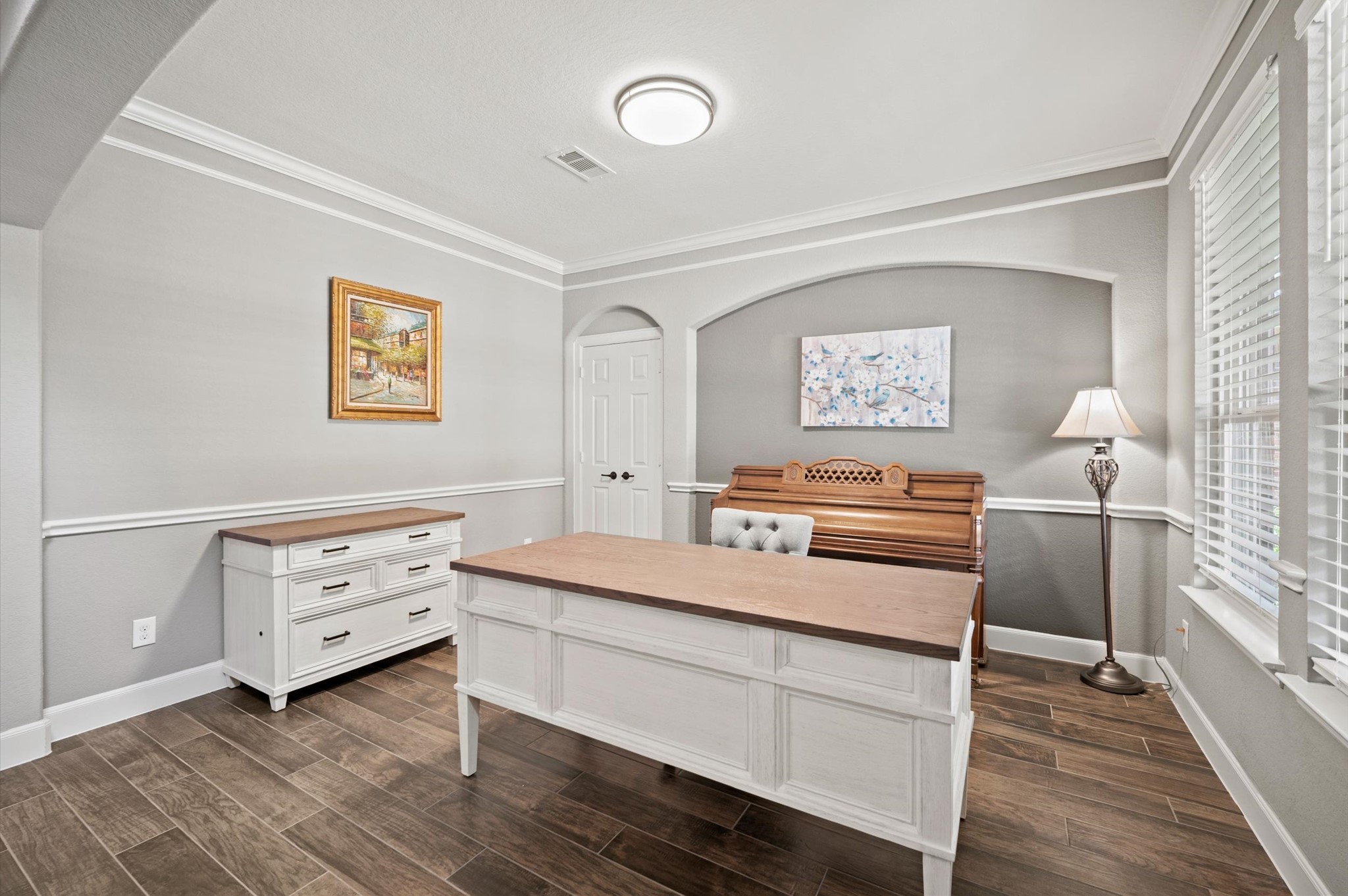 9507 Empress Crossing Drive Spring, TX 77379 - Photo 9 of 50 This room features elegant hardwood flooring, soft gray walls with white trim, and large windows for natural light. It includes a stylish white desk and a classic piano, ideal for a home office or music room.