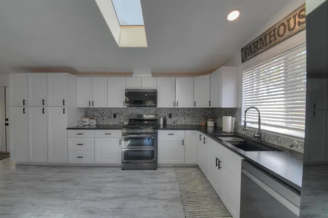 a kitchen with granite countertop white cabinets stainless steel appliances a sink and a window