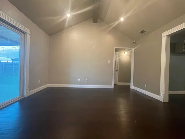 an empty room with wooden floor and windows with curtains