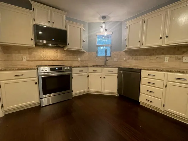 a kitchen with stainless steel appliances granite countertop a stove a sink and white cabinets