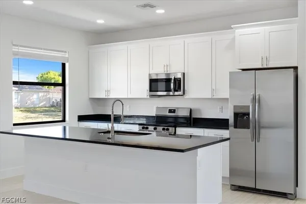 a kitchen with stainless steel appliances granite countertop a refrigerator a stove a sink and white cabinets with wooden floor