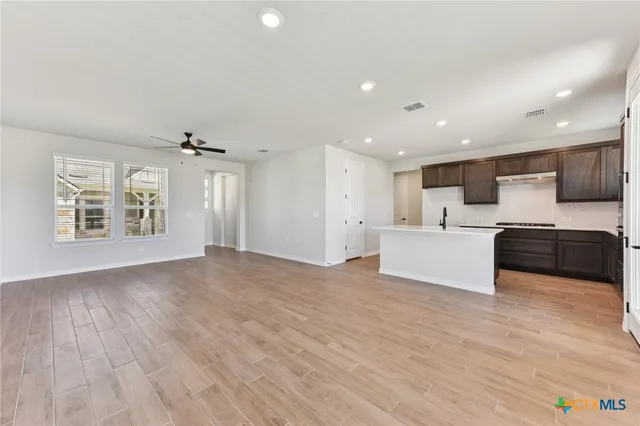 a view of an empty room with wooden floor and a ceiling fan