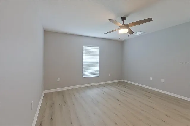 an empty room with wooden floor fan and windows