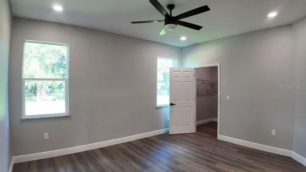 an empty room with wooden floor fan and windows