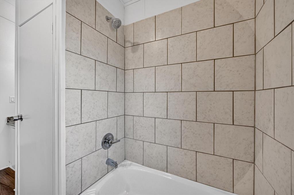 246 PR-4443 Rhome, TX 76078 - Photo 24 of 35 White bathtub with a chrome showerhead and faucet, surrounded by light-toned rectangular wall tiles
