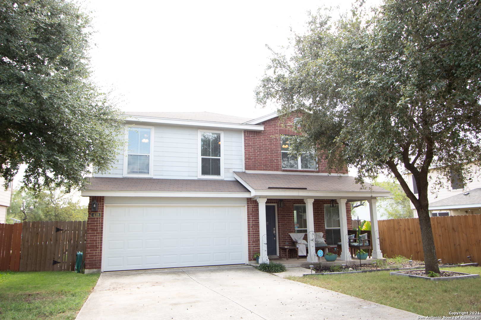 a view of a white house with a large tree and wooden fence