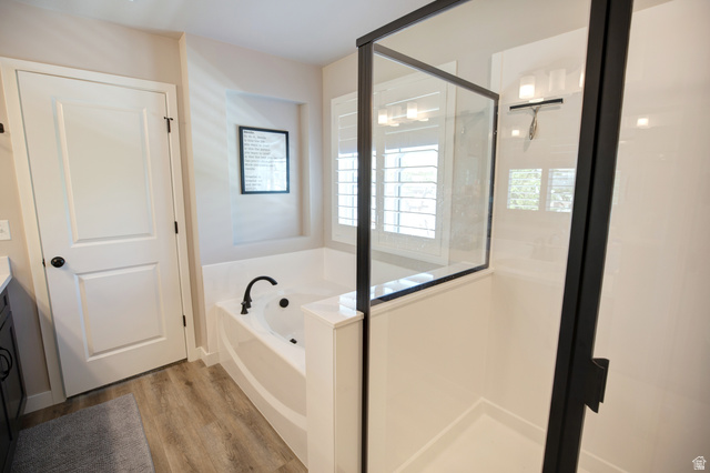 983 South 950 West Provo, UT 84601 - Photo 18 of 56 Modern bathroom with a spacious soaking tub featuring a matte black faucet, a separate glass-enclosed shower with black framing, wood-finish flooring, and white plantation shutters