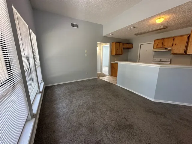 an empty room with windows and view of kitchen