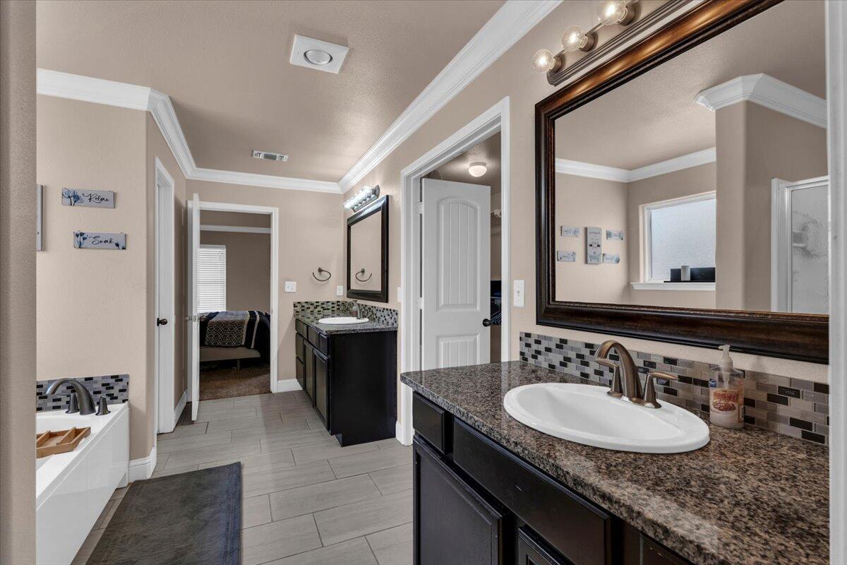 3641 Ridgely Avenue Lubbock, TX 79407 - Photo 15 of 32 a en suite bathroom with a granite countertop sink a mirror a bathtub and shower