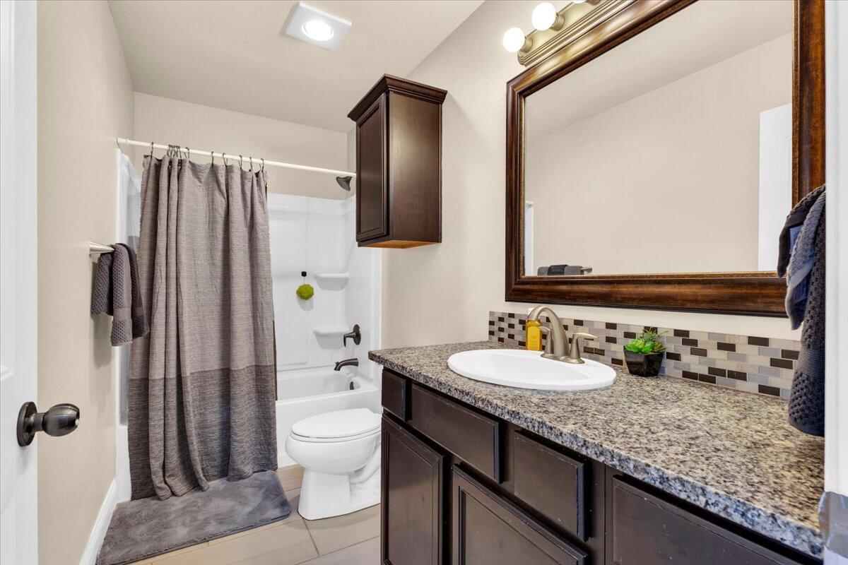 3641 Ridgely Avenue Lubbock, TX 79407 - Photo 19 of 32 a bathroom with a granite countertop sink a toilet a mirror and shower