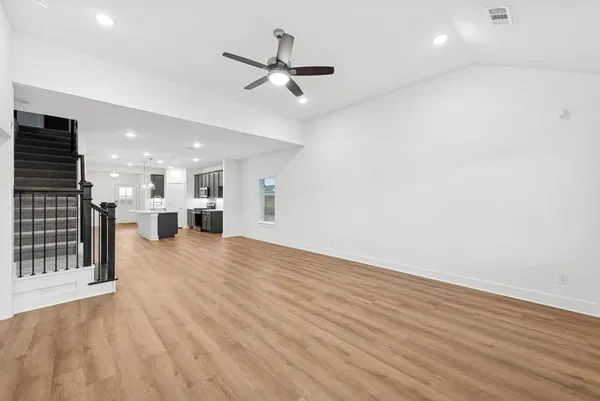 an empty room with wooden floor a ceiling fan and windows