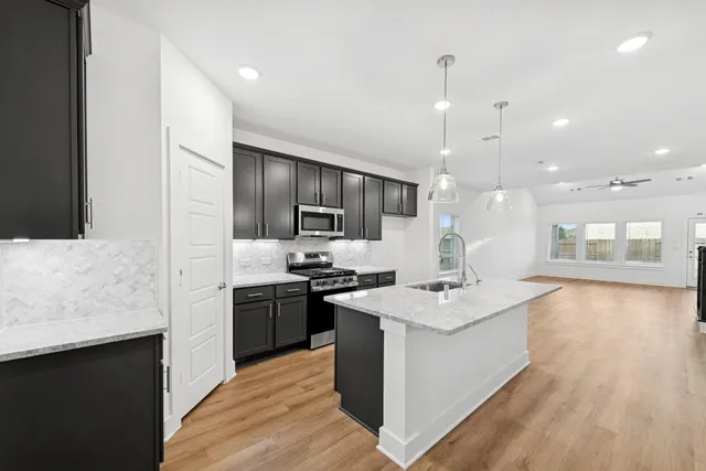a kitchen with stainless steel appliances kitchen island a sink dishwasher a stove and a refrigerator with wooden floor