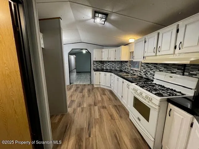 a kitchen with granite countertop a stove a sink dishwasher and white cabinets with wooden floor