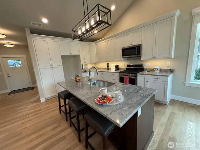 a kitchen with stainless steel appliances granite countertop a stove refrigerator a microwave oven a sink dishwasher and white cabinets with wooden floor