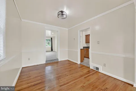 a view of empty room with wooden floor and kitchen
