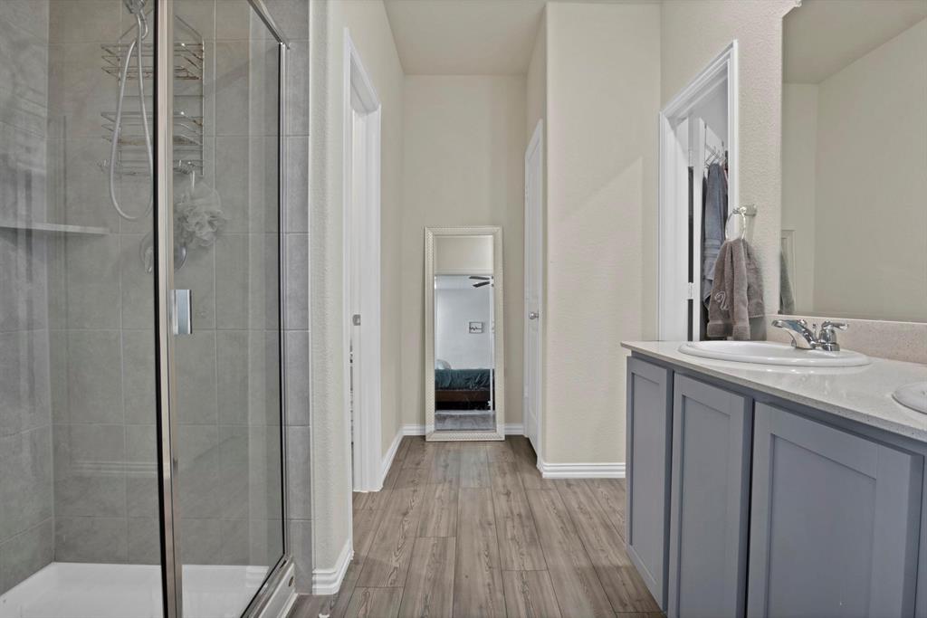 621 Ridgeback Trail Fort Worth, TX 76052 - Photo 11 of 22 Bathroom featuring a glass-enclosed shower with tile surround, wood-finish flooring, a double vanity with light gray cabinetry, and a light-toned countertop